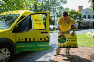 Mosquito Joe of Central Indianapolis technician placing a yard sign in front of a Mosquito Joe transit van.
