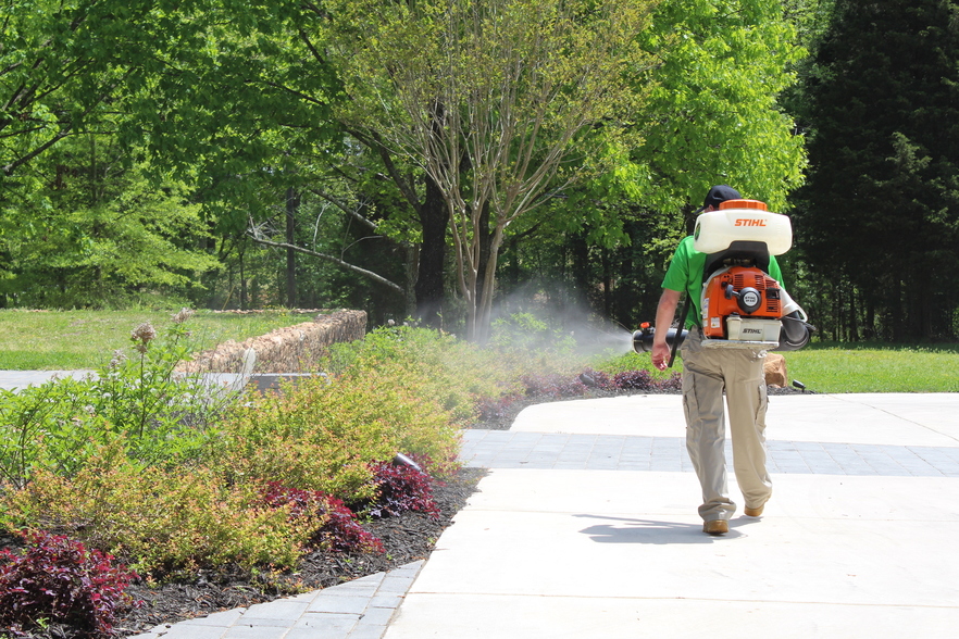 A Mosquito Joe technician sprays barrier treatment on shrubbery on an Indiana lawn.